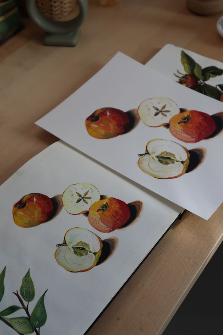 High-quality paintings of apples on paper sheets arranged on a wooden table, showcasing fruit art.